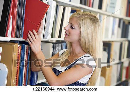 Picture - Woman in library pulling book off a shelf (depth of field). Fotosearch