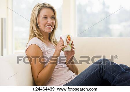 Stock Photo - Woman in living room with coffee smiling. Fotosearch