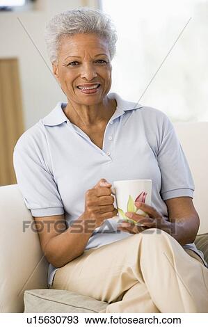 Woman sitting in living room with coffee smiling View Large Photo Image Stock Image - Woman sitting in living room with coffee smiling. Fotosearch
