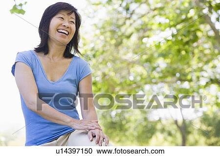 Stock Image - Woman sitting outdoors smiling. Fotosearch