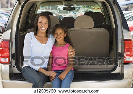 Stock Image - Woman with young girl sitting in back of van smiling. Fotosearch