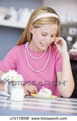 Stock Photograph - Young woman sitting at a table eating a sweet treat. Fotosearch