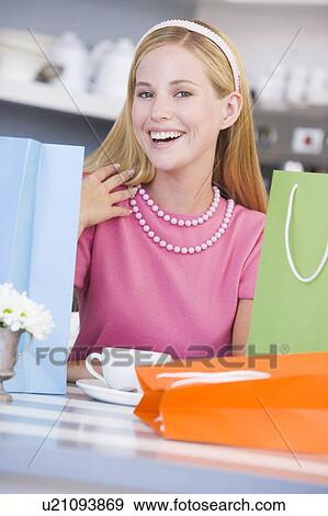 Young woman sitting at a table taking a break from shopping View Large Photo Image Stock Photo - Young woman sitting at a table taking a break from shopping. Fotosearch