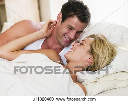 Stock Image - Couple lying in bed smiling. Fotosearch