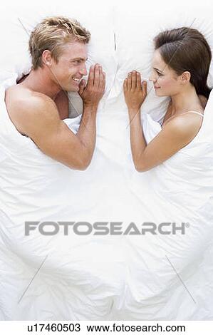 Stock Image - Couple lying in bed smiling. Fotosearch