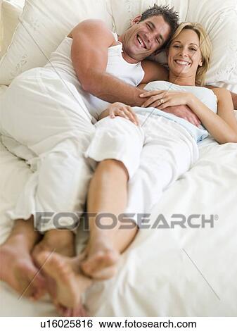 Stock Photograph - Couple lying in bed smiling. Fotosearch