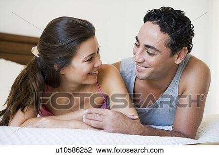 Stock Image - Couple relaxing on bed in bedroom smiling (selective focus). Fotosearch