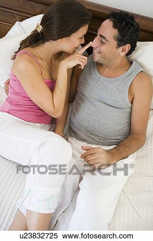 Stock Photography - Couple relaxing on bed in bedroom bonding and smiling (selective focus). Fotosearch
