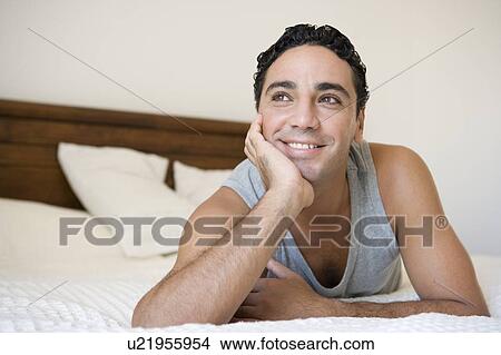 Man relaxing on bed in bedroom smiling (selective focus) View Large Photo Image Picture - Man relaxing on bed in bedroom smiling (selective focus). Fotosearch