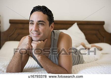 Stock Photo - Man relaxing on bed in bedroom smiling (selective focus). Fotosearch