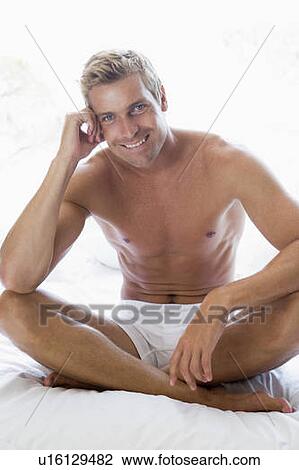 Stock Image - Man sitting on bed smiling. Fotosearch
