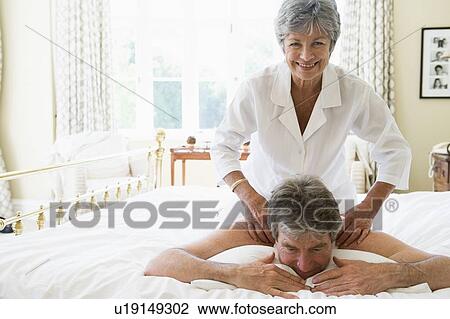 Stock Image - Woman giving man massage in bedroom smiling. Fotosearch