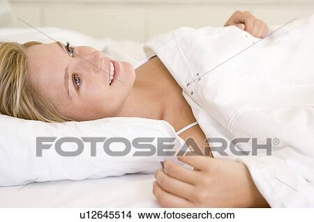 Woman lying in bed smiling View Large Photo Image Picture - Woman lying in bed smiling. Fotosearch