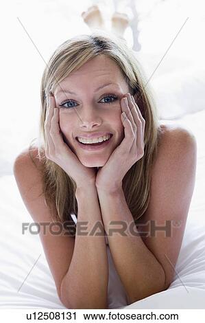 Stock Image - Woman lying in bed smiling. Fotosearch