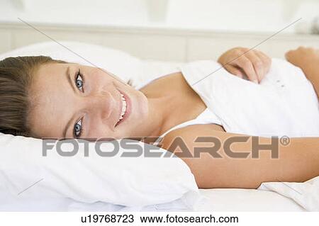 Stock Image - Woman lying in bed smiling. Fotosearch