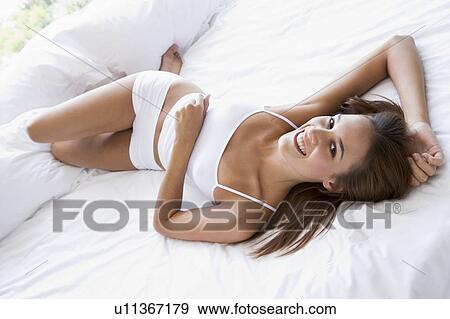 Stock Photo - Woman lying in bed smiling. Fotosearch