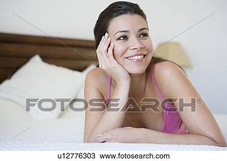 Stock Image - Woman relaxing on bed in bedroom smiling (selective focus). Fotosearch