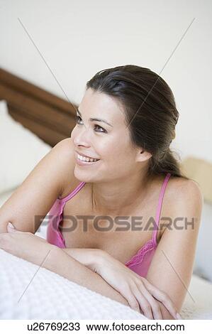Stock Image - Woman relaxing on bed in bedroom smiling (selective focus). Fotosearch