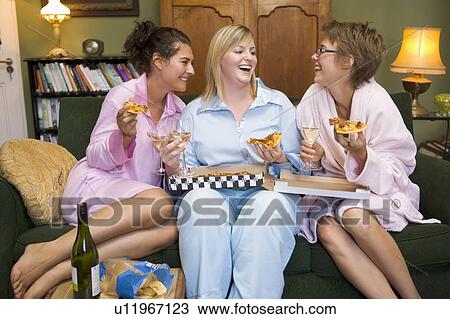 Stock Image - Three woman in night clothes sitting at home eating pizza. Fotosearch