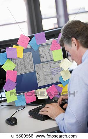 Businessman in office typing at computer with notes on it View Large Photo Image Stock Photograph - Businessman in office typing at computer with notes on it. Fotosearch