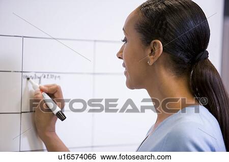 Stock Photograph - Businesswoman indoors writing on erasable board. Fotosearch