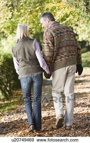 Stock Photo - Couple outdoors walking on path in park holding hands and smiling (selective focus). Fotosearch