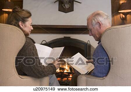 Couple sitting in living room by fireplace reading View Large Photo Image Stock Photo - Couple sitting in living room by fireplace reading. Fotosearch