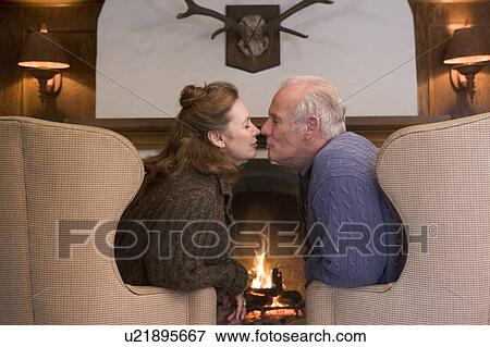 Stock Photo - Couple sitting in living room by fireplace kissing. Fotosearch