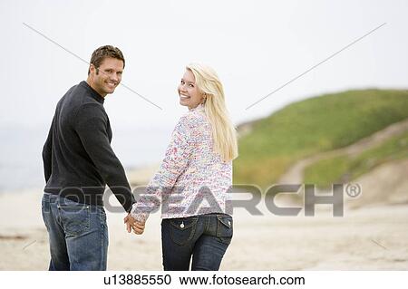 Couple walking at beach holding hands smiling View Large Photo Image Stock Image - Couple walking at beach holding hands smiling. Fotosearch