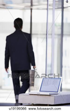 Stock Photograph - Laptop sitting on stone bench outdoors with businessman walking away in background (high key/selective focus). Fotosearch