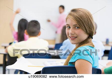 Stock Image - Student in class looking at camera with teacher in background (selective focus). Fotosearch