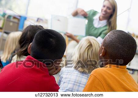 Stock Image - Students in class with teacher reading to them (depth of field). Fotosearch