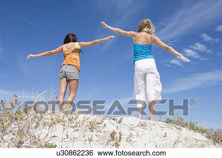 Two young women posing on a sand hill View Large Photo Image Stock Photograph - Two young women posing on a sand hill. Fotosearch