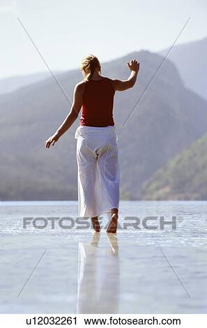 Stock Image - Woman outdoors walking on water in scenic location. Fotosearch
