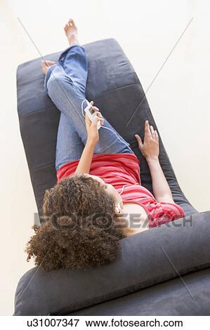 Stock Photo - Woman sitting in chair listening to MP3 player. Fotosearch