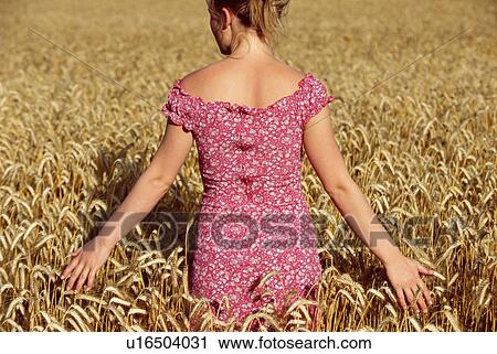 Stock Image - Woman standing outdoors in wheat field (selective focus). Fotosearch