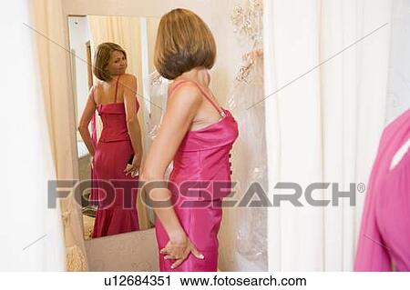 Stock Image - Woman trying on dresses and frowning. Fotosearch