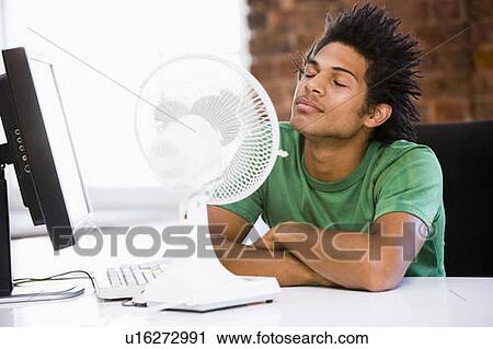 Stock Image - Businessman in office with computer and fan cooling off. Fotosearch