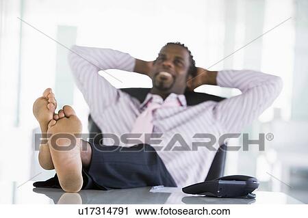 Businessman sitting in office with feet on desk relaxing and smiling View Large Photo Image Stock Image - Businessman sitting in office with feet on desk relaxing and smiling. Fotosearch