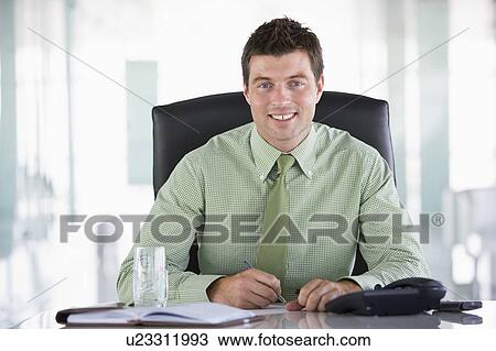 Stock Image - Businessman sitting in office with personal organizer smiling. Fotosearch
