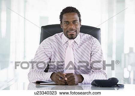 Stock Image - Businessman sitting in office with personal organizer smiling. Fotosearch