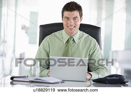 Businessman sitting in office with personal organizer using laptop smiling View Large Photo Image Stock Photo - Businessman sitting in office with personal organizer using laptop smiling. Fotosearch