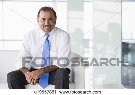 Businessman sitting indoors smiling (high key/selective focus) View Large Photo Image Stock Image - Businessman sitting indoors smiling (high key/selective focus). Fotosearch