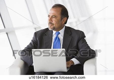 Businessman sitting indoors with laptop looking out window (high key/selective focus) View Large Photo Image Stock Photograph - Businessman sitting indoors with laptop looking out window (high key/selective focus). Fotosearch