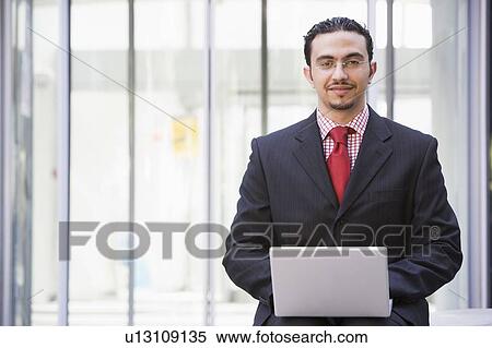 Businessman sitting outdoors by building with a laptop smiling (high key/selective focus) View Large Photo Image Stock Photography - Businessman sitting outdoors by building with a laptop smiling (high key/selective focus). Fotosearch