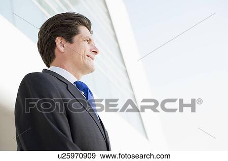 Businessman standing outdoors by building smiling View Large Photo Image Stock Photo - Businessman standing outdoors by building smiling. Fotosearch