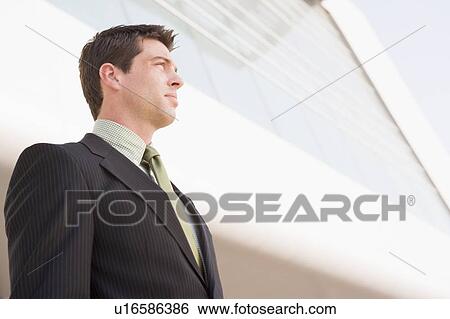 Stock Photograph - Businessman standing outdoors by building. Fotosearch