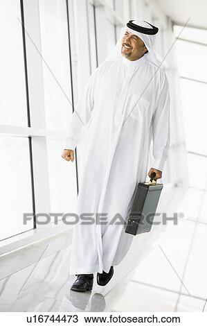 Stock Image - Businessman walking in a corridor with a briefcase smiling (high key/selective focus). Fotosearch