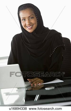 Stock Photo - Businesswoman in office with laptop smiling (high key/selective focus). Fotosearch