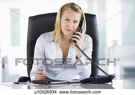 Picture - Businesswoman in office with personal organizer open on telephone. Fotosearch